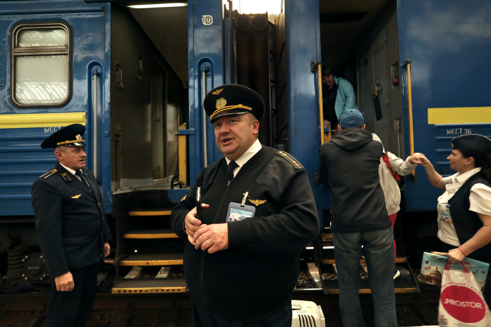 Two men in uniform and hat flank a set of steps on a blue train car