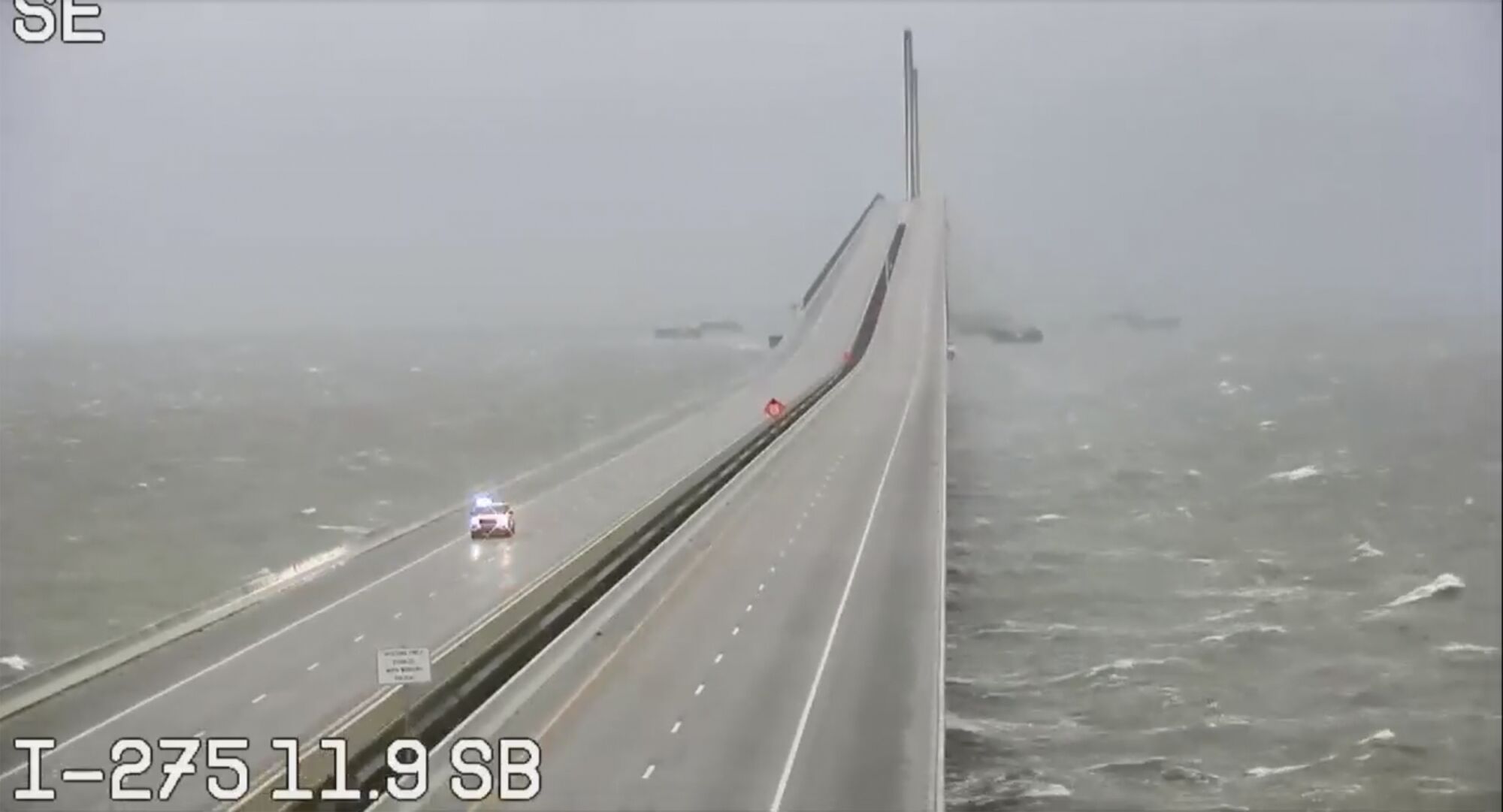 An emergency vehicle is the only automobile on a causeway as whitecaps churn below