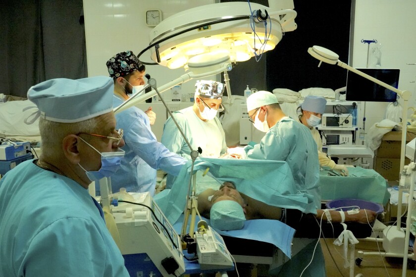 Doctors in masks and light-blue scrubs work on a man lying on a table under a bright light amid medical equipment