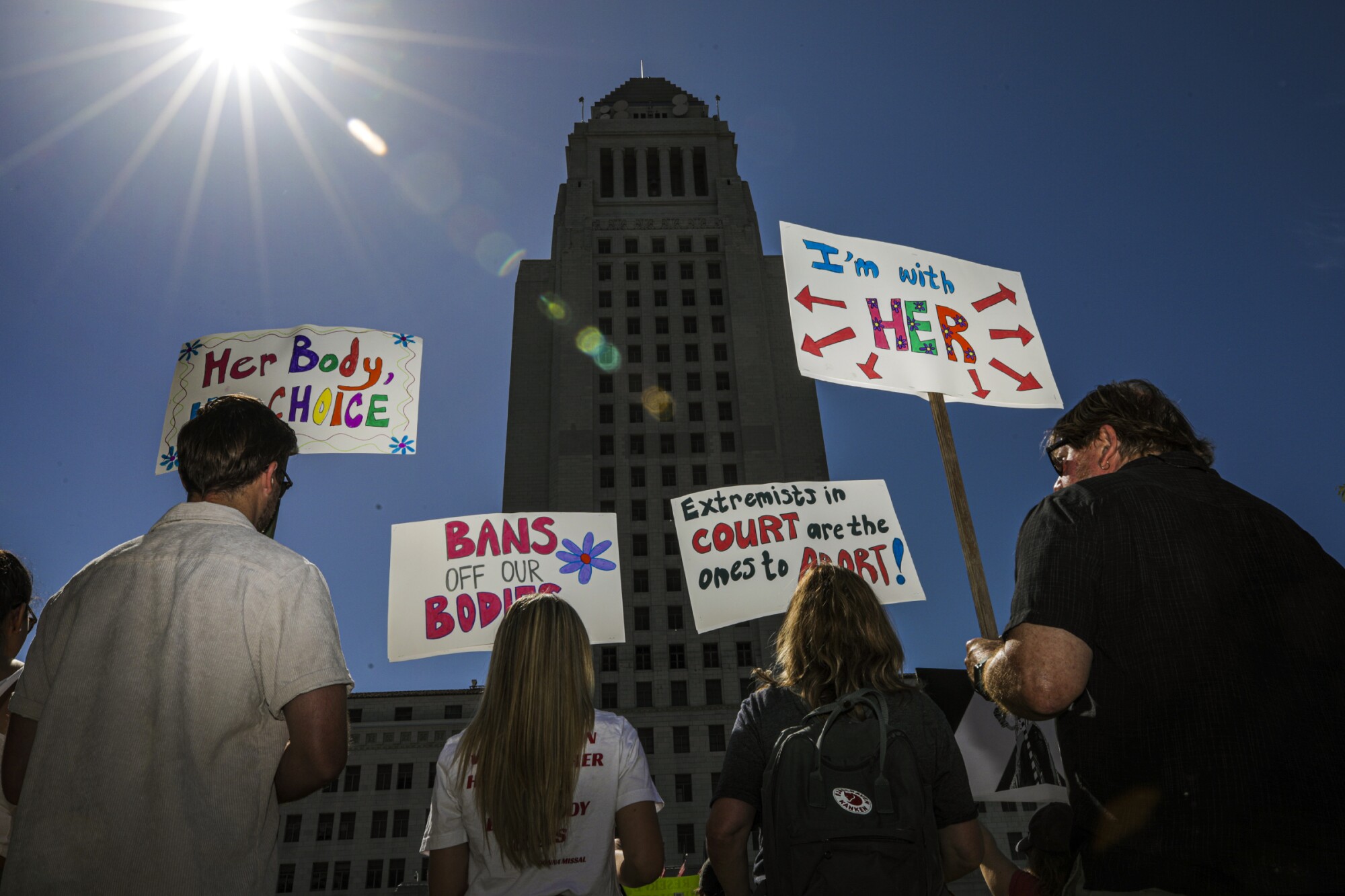 People hold signs at an abortion rights rally in downtown L.A. that read, "I'm with her" and "Bans off our bodies."