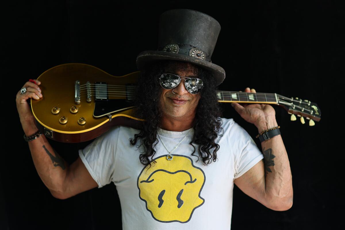 Slash wears his trademark top hat and holds a guitar on his shoulders behind his head