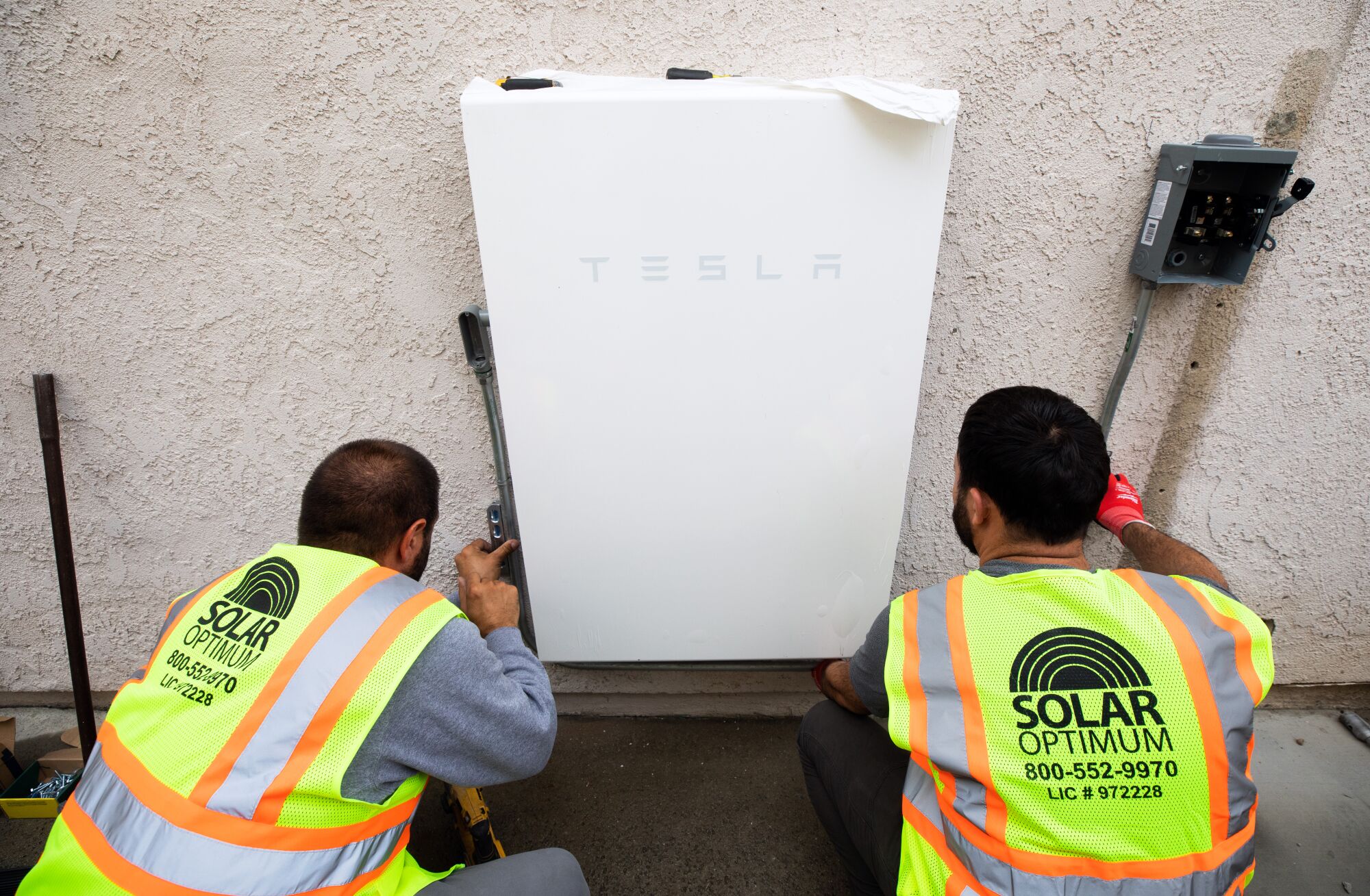 Solar Optimum installers set up a Tesla Powerwall battery system during a solar panels installation at a house in Brea.
