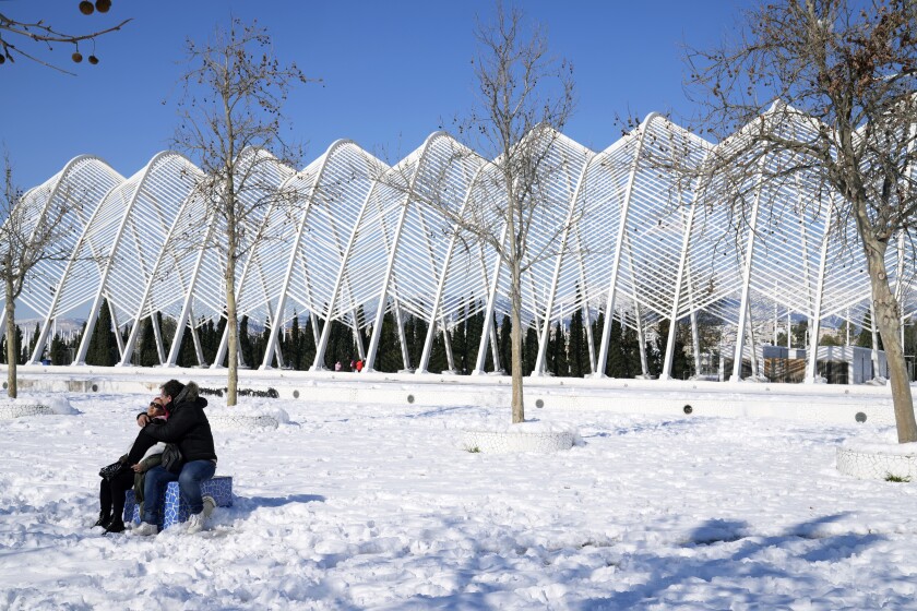A woman and a man enjoy snow at the main Olympic complex, in northern Athens, Greece, Wednesday, Jan. 26, 2022. Greek authorities struggle to clear blocked roads and restore power to blacked out parts of the Greek capital after heavy snowfall has caused major disruptions in Greece. (AP Photo/Thanassis Stavrakis)
