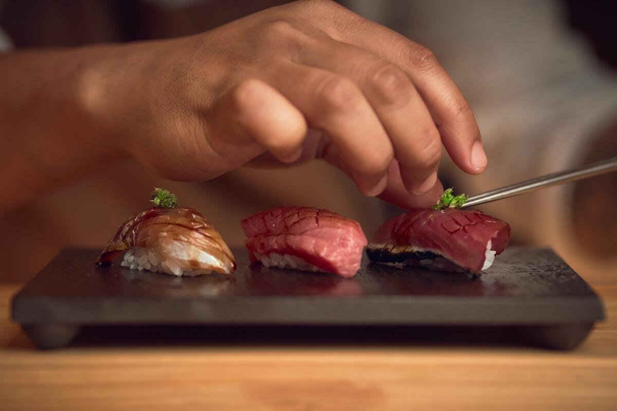 A close-up of three nigiri being prepared by hand and with tweezers