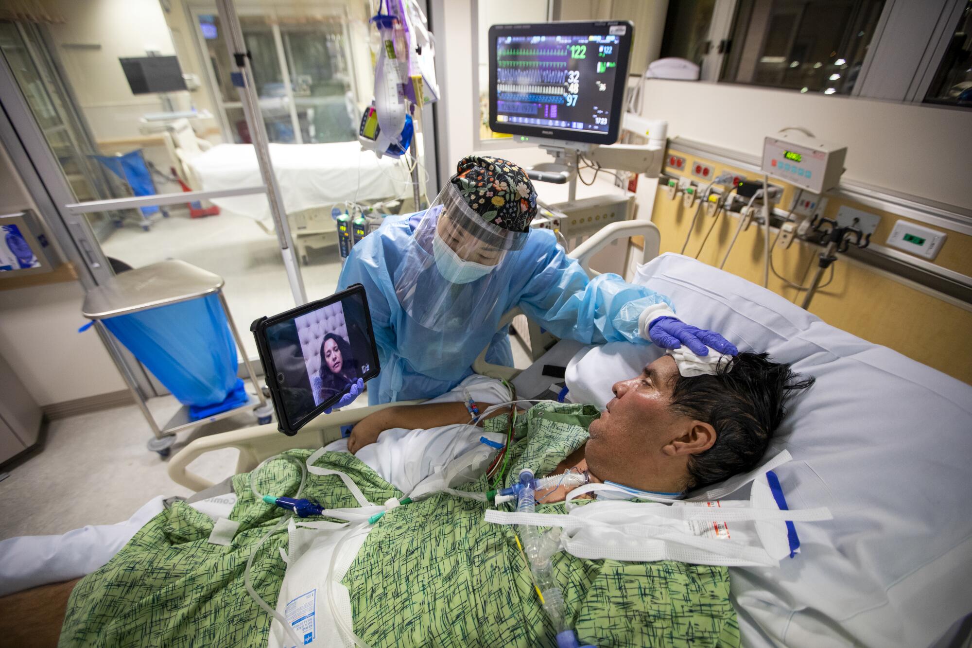 Registered Nurse Kat Yi holds an iPad up to Eduardo Rojas inside the ICU at Providence St. Jude Medical Center.