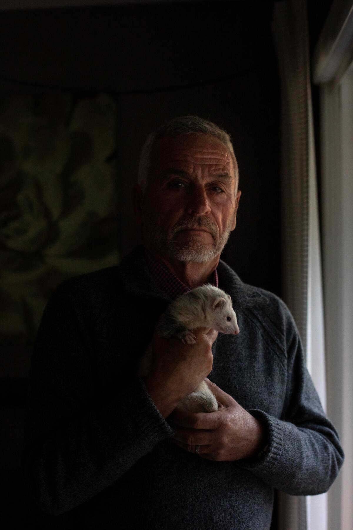 A man holding a ferret beside a window