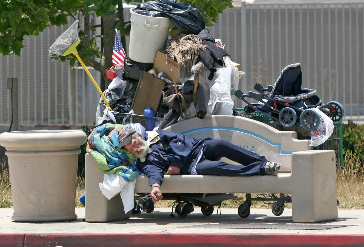 A homeless man sleeps on a city bench on Harbor Boulevard in Costa Mesa.