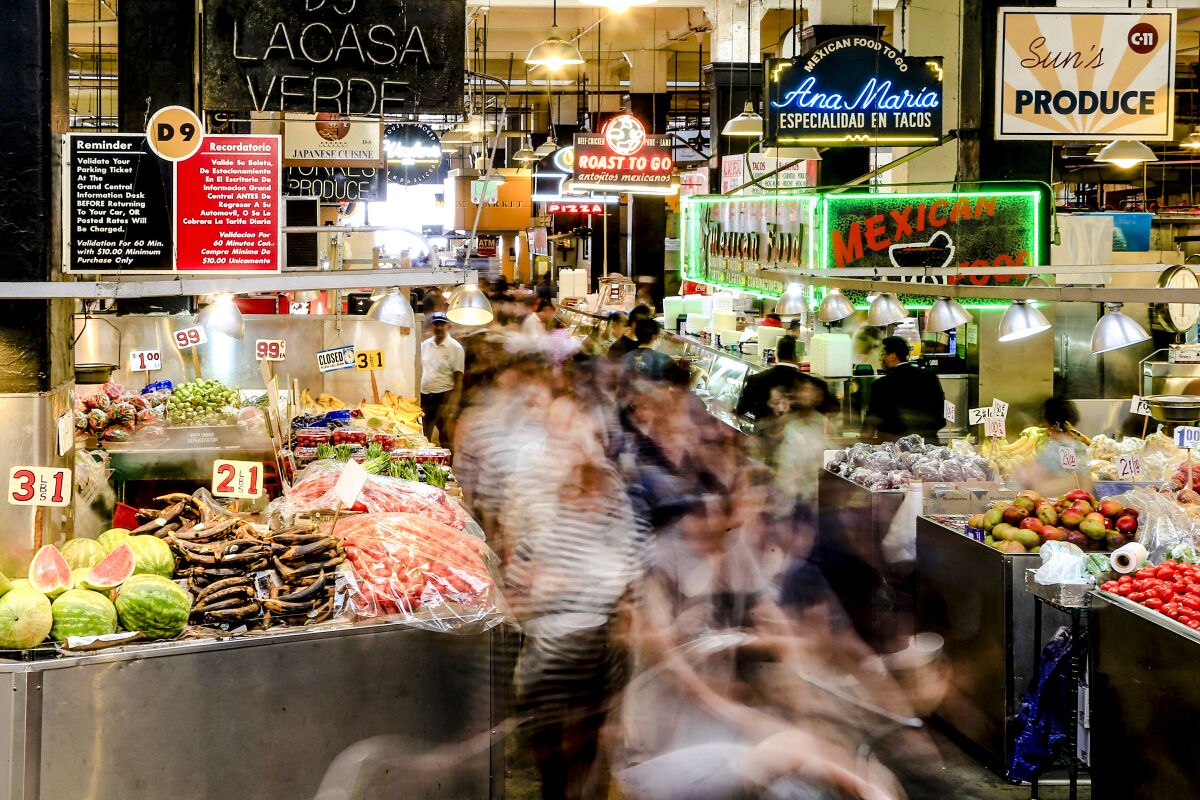 People blur in front of vegetable and fruit stands at an indoor market.
