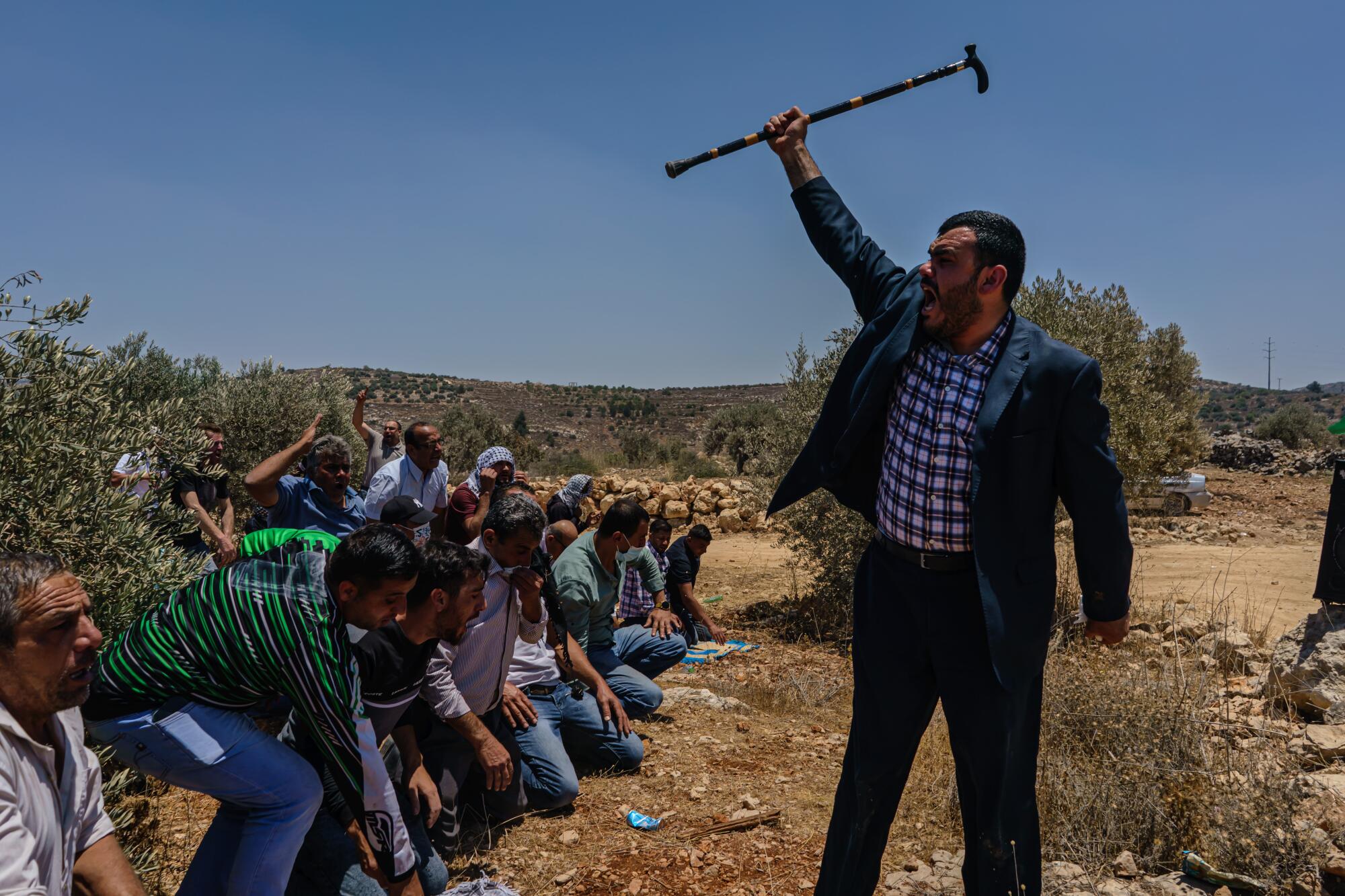 A Palestinian man leading the Friday prayers raises his walking stick in a call to arms after they were tear gassed.
