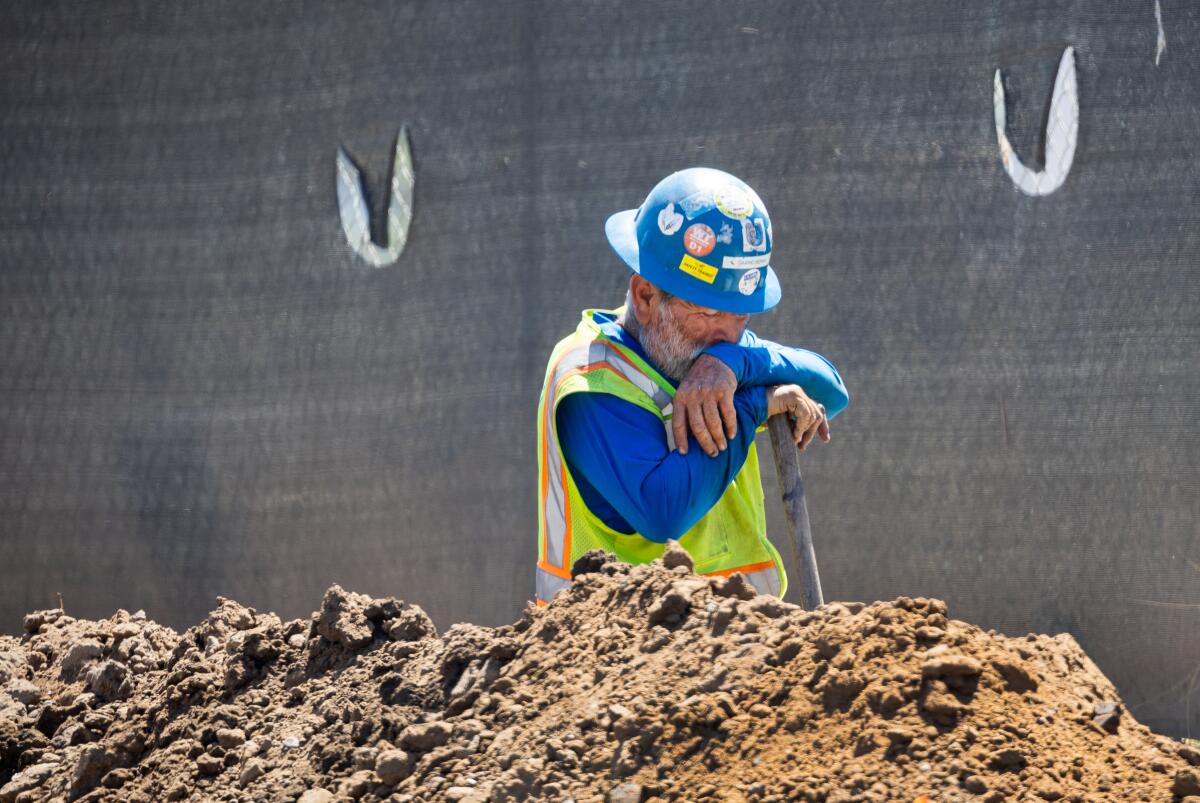 A construction worker taking a quick break while digging a trench with a shovel amid a heat wave.