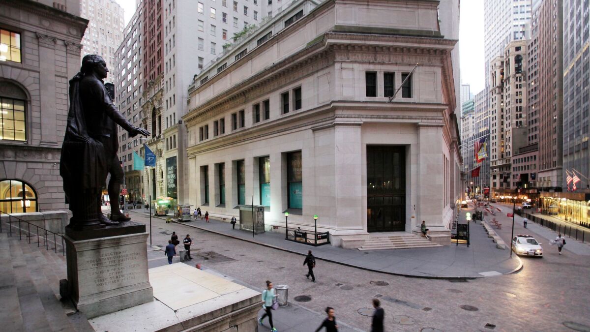 Pedestrians on Wall Street beneath a statue of George Washington.