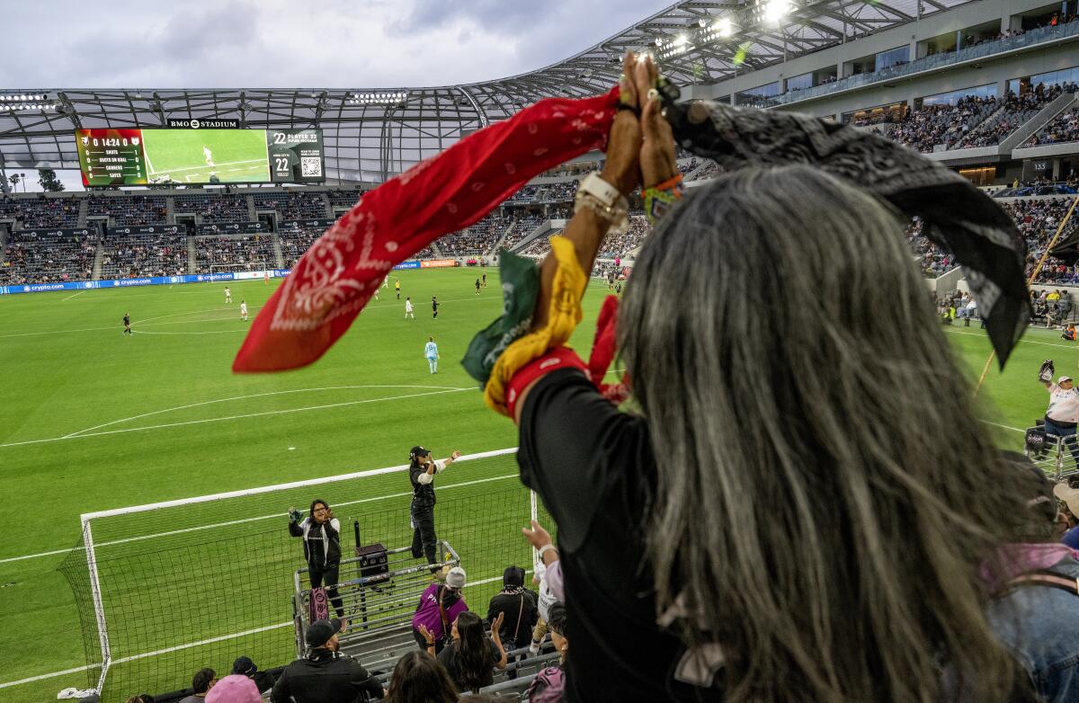 View of a woman standing in soccer stadium seating holding bandanas from the back.