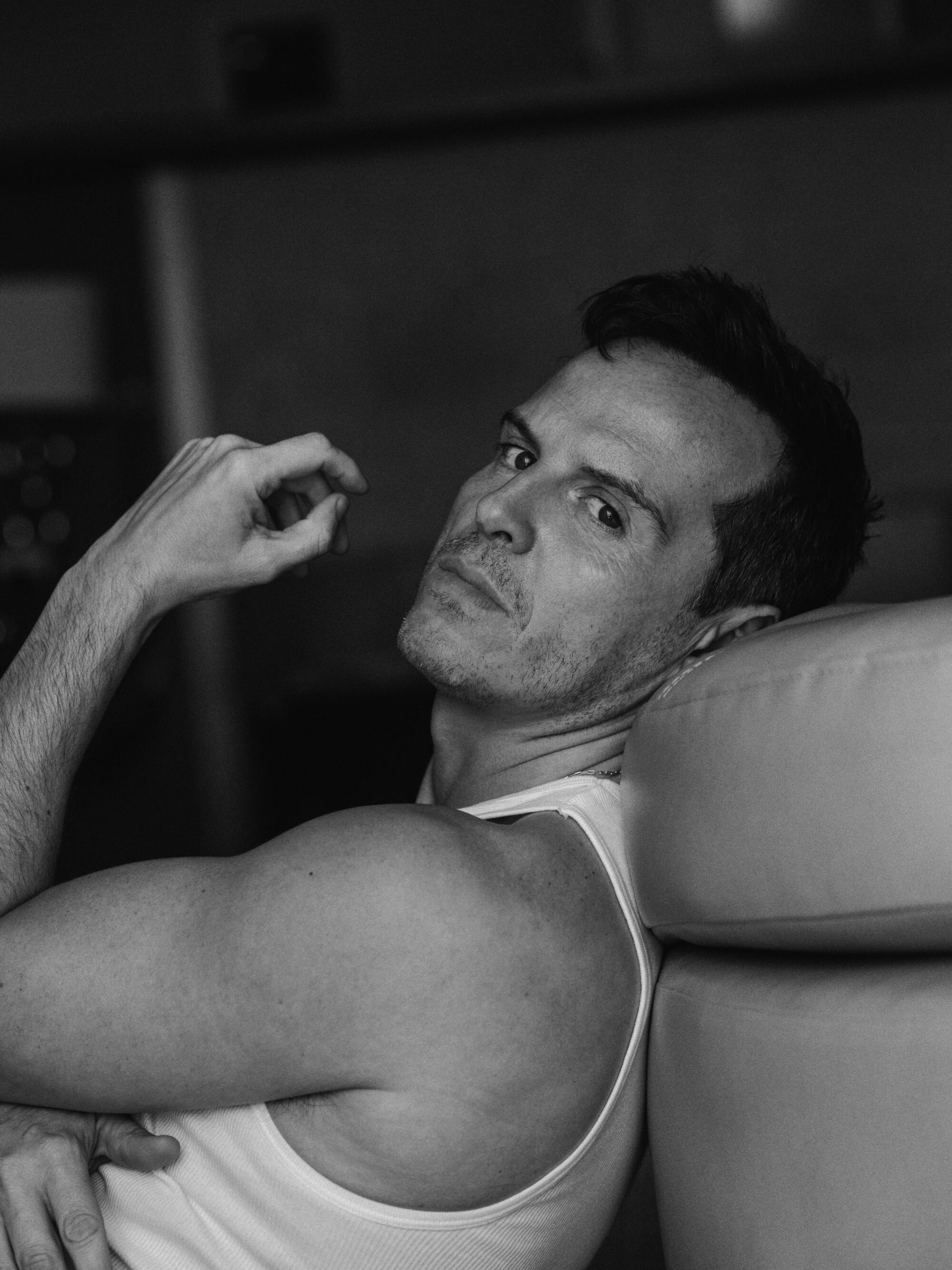 Andrew Scott sits on the floor and leans against the sofa in a black-and-white portrait.