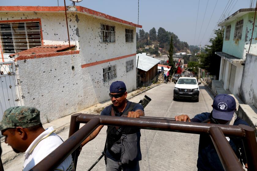 Members of the United Front of Community Police of Guerrero pass by bullet-riddled homes in Filo de Caballos, Guerrero, on April 25, 2019.