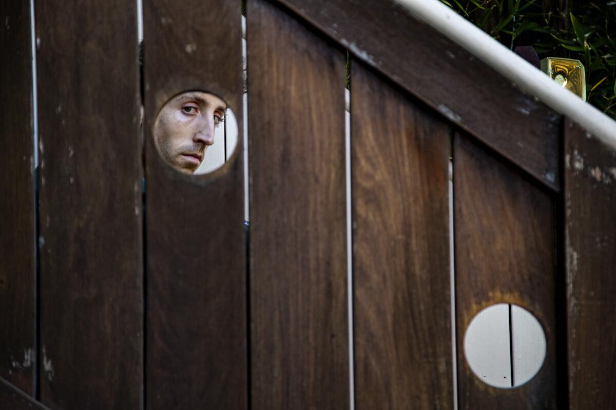 Sam Gendel's face is seen through a hole in wooden boards.