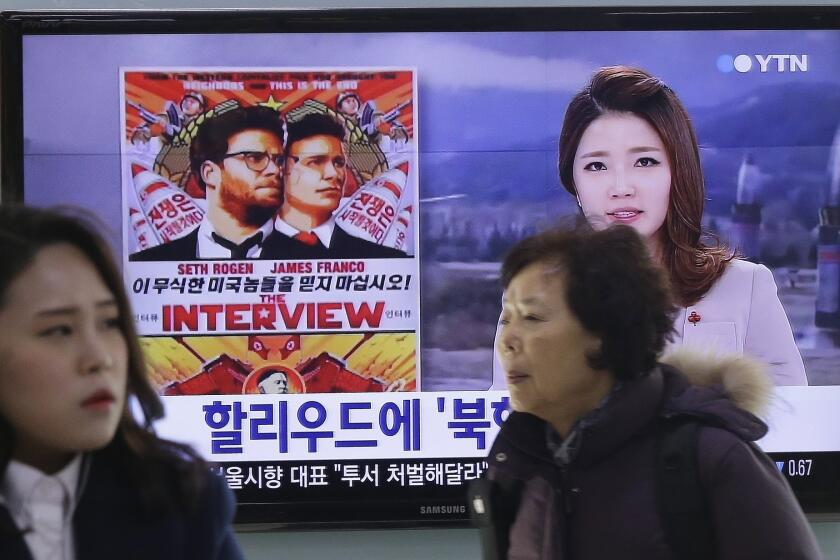 People at the Seoul Railway Station walk past a TV screen showing a poster for Sony Pictures' "The Interview." President Obama has pledged to respond to the cyberattack that led the studio to cancel the North Korea-themed movie's release.