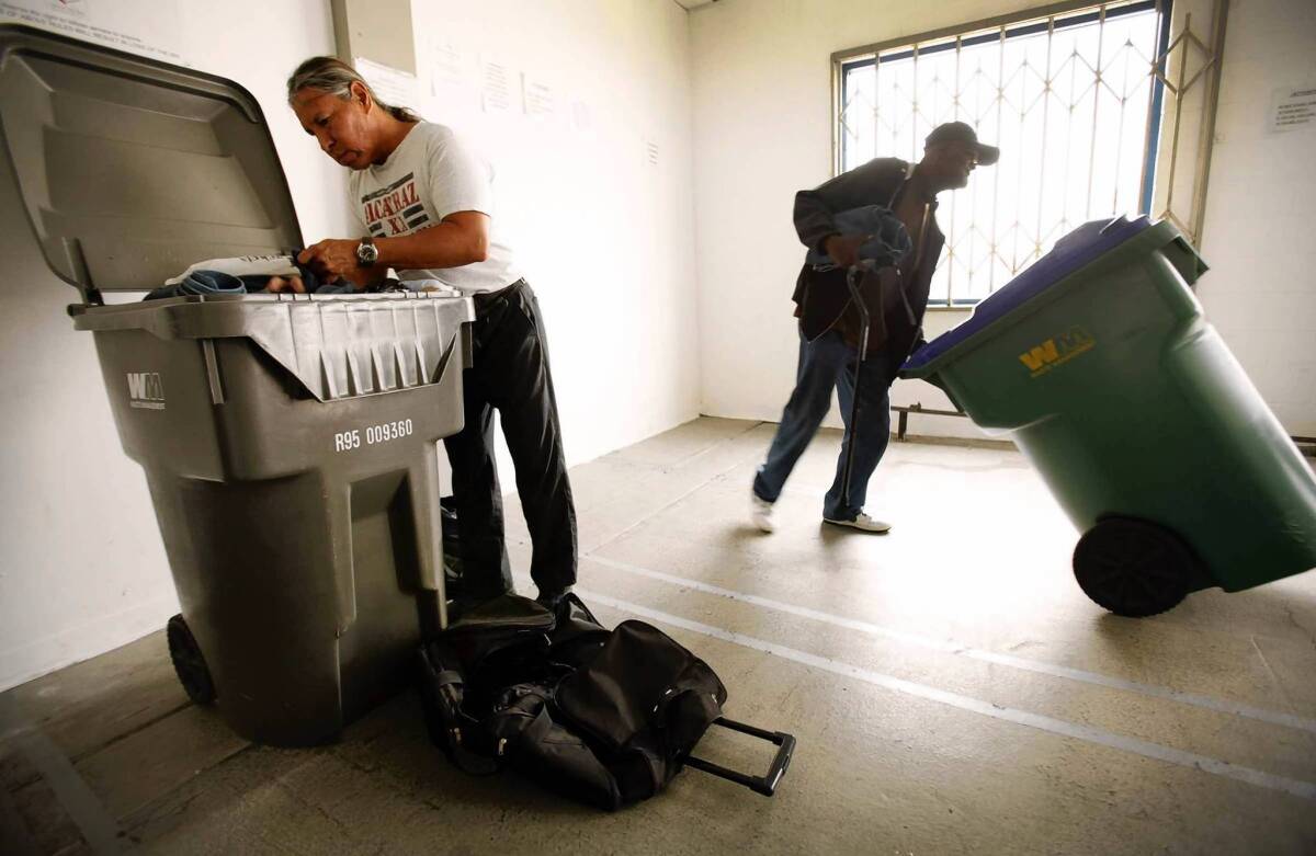 Newton Burr, left, organizes his belongings in a converted trash bin while Ed Richmond, right, wheels his bin back to the storage area at the downtown Los Angeles Check-In Center, which is operated by the Central City East Assn. business improvement district and provides homeless residents a place to keep their things. Cash-strapped cities throughout California are struggling with the spread of encampments and the ramifications of clearing them out.