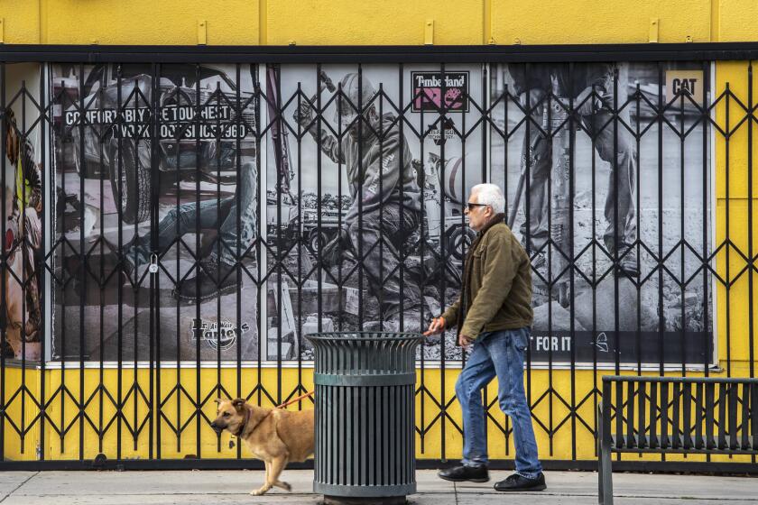 CANOGA PARK, CA - APRIL 08: A man walks his dog past a shuttered shoe store as the coronavirus and extended stay-at-home orders are closing every non-essential business in the community on Sherman Way on Wednesday, April 8, 2020 in Canoga Park, CA. (Brian van der Brug / Los Angeles Times)