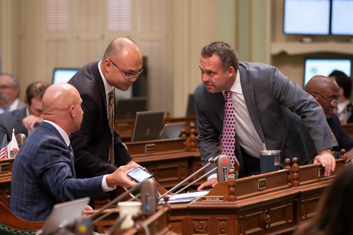 Three men in suits and ties lean over an ornate wooden desk