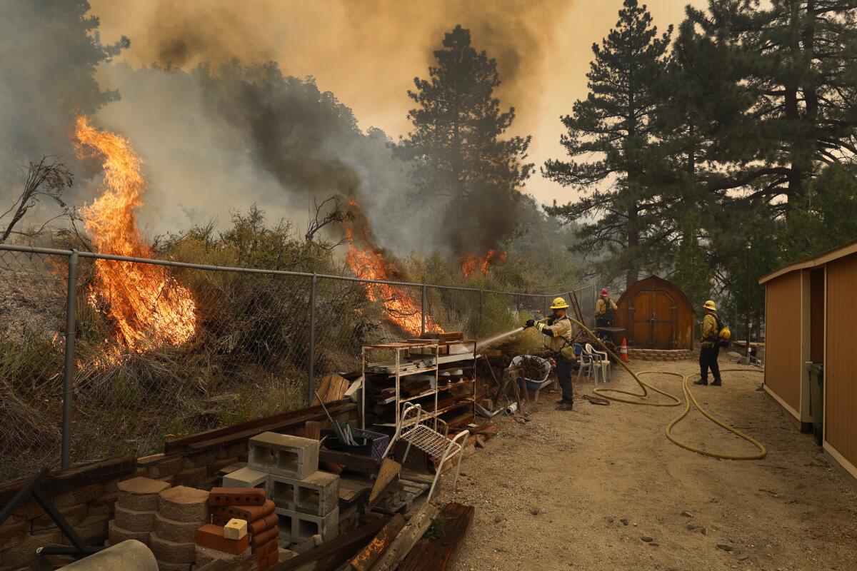 Firefighters spray water as flames approach a property.