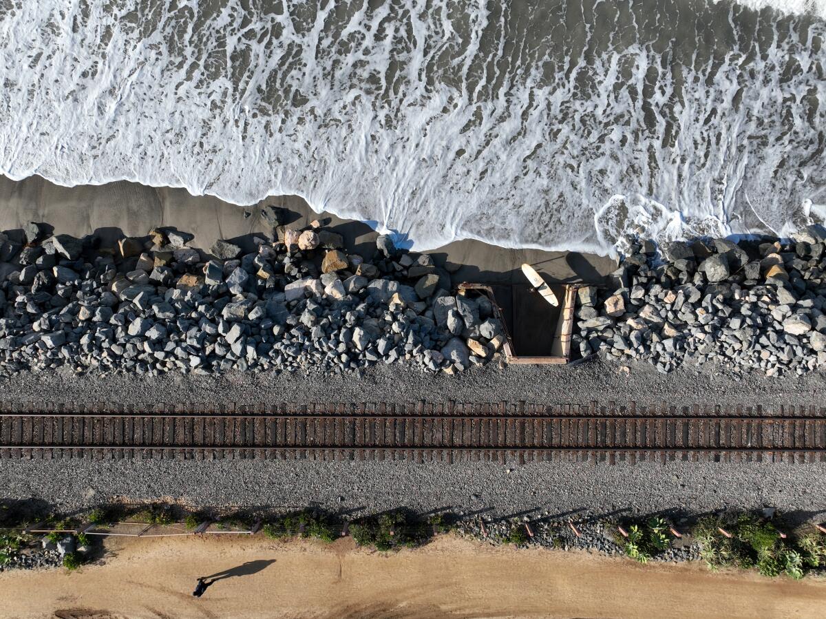 A surfer heads in near the train tracks, north of the San Clemente Pier in March