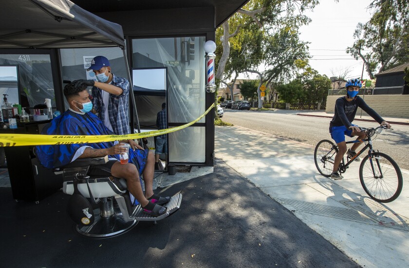 A barber gives a haircut under a canopy outside his shop as a bicyclist rides past