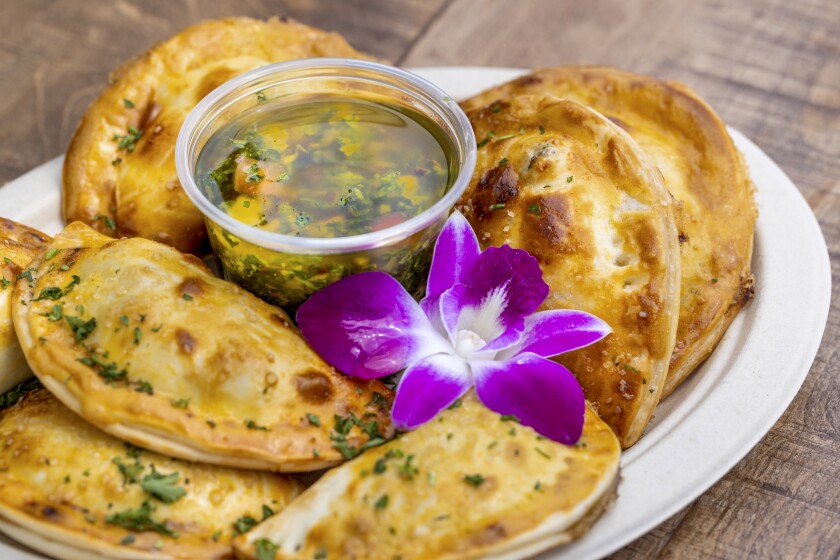 A photo of a plate of Empanadas decorated with a purple orchid.