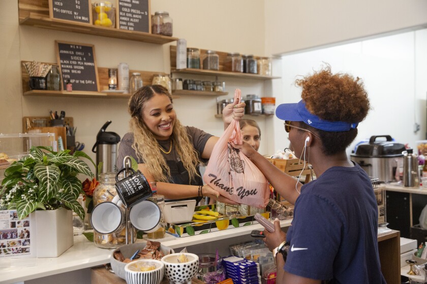 LaRayia Gaston hands groceries to customer Kendall Young at LaRayia’s Bodega