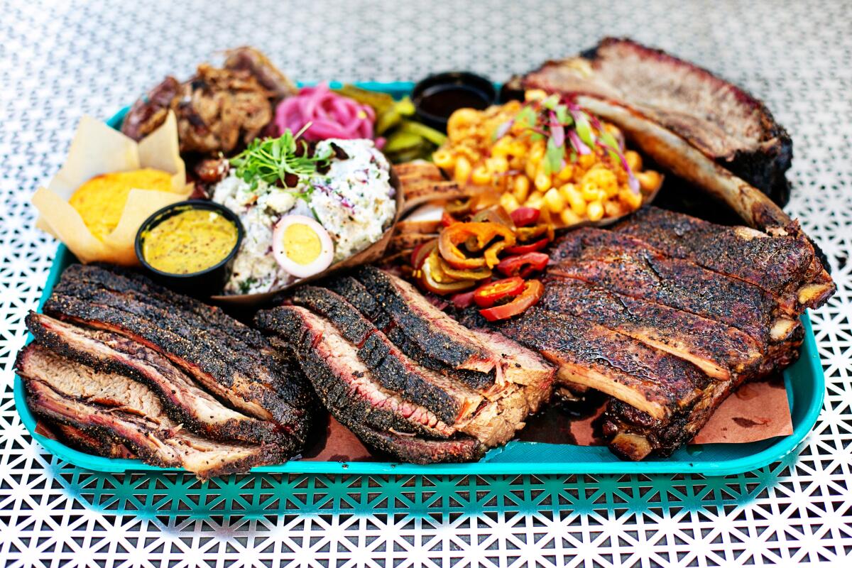 Una bandeja turquesa de carne y lados a la parrilla, como pan de maíz y salsa de barbacoa