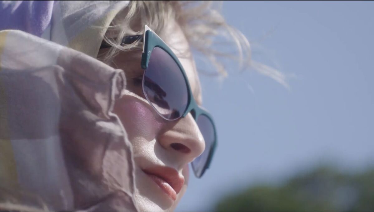 A closeup of a person wearing sunglasses and a head scarf.