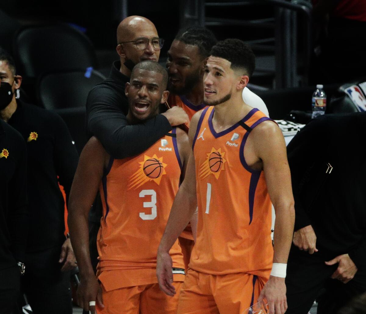 Suns Coach Monty Williams hugs guard Chris Paul as teammate Devin Booker, right, stands nearby.
