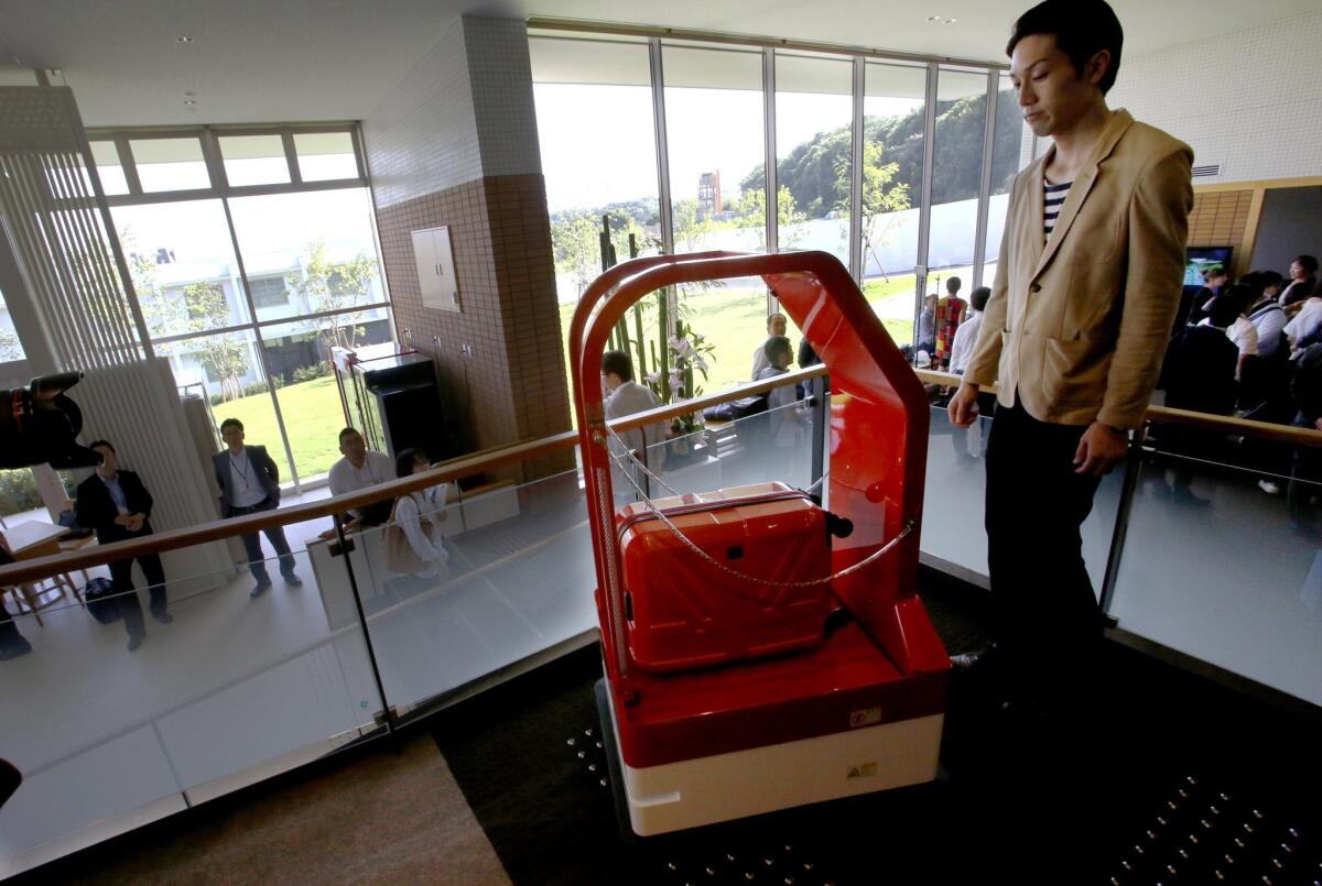 A porter robot, left, escorts a hotel employee during a demonstration for the media at the new hotel, aptly called Henn na Hotel or Weird Hotel, in Sasebo, southwestern Japan, Wednesday, July 15, 2015. From the receptionist that does the check-in and check-out to the porter that's a stand-on-wheels taking luggage up to the room, the hotel, that is run as part of Huis Ten Bosch amusement park, is "manned" almost totally by robots to save labor costs. (AP Photo/Shizuo Kambayashi)