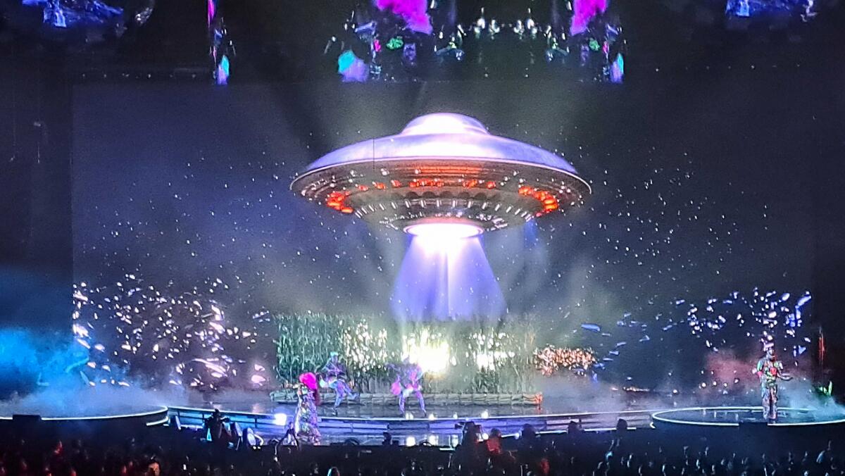 An image of a flying saucer hovers over a concert stage.