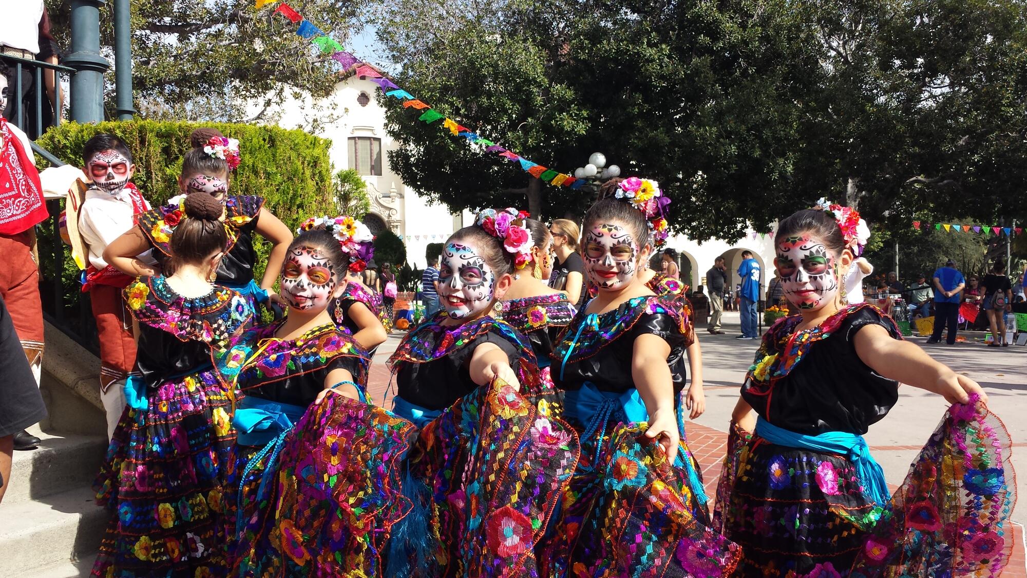 Four young girls dressed in traditional dresses with their faces painted as calaveras.