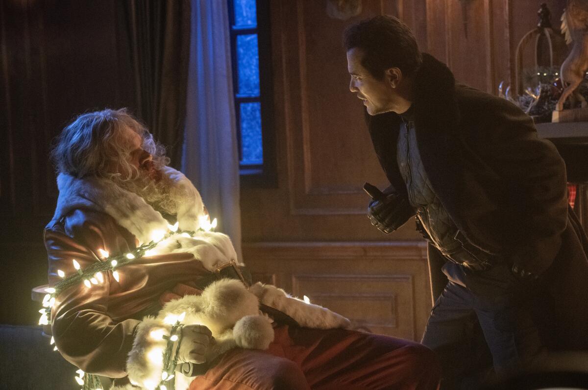 David Harbour in a Santa suit is wrapped in holiday lights and John Leguizamo is bending over him in "Violent Night."