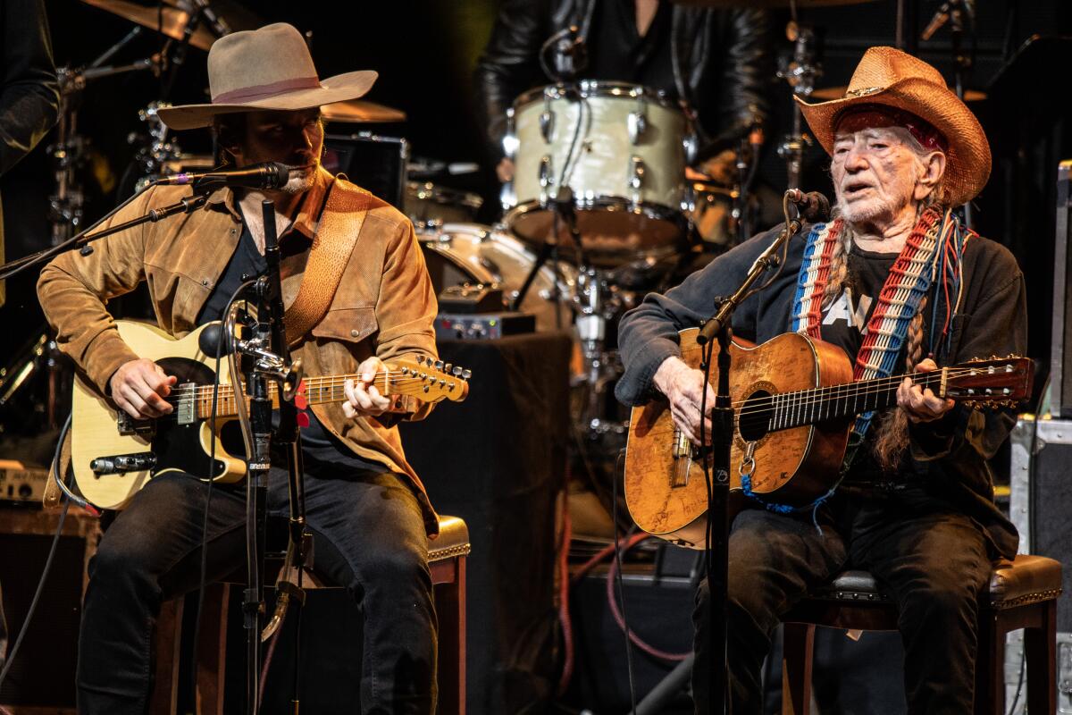 Willie Nelson and his son Lukas seated playing guitars onstage