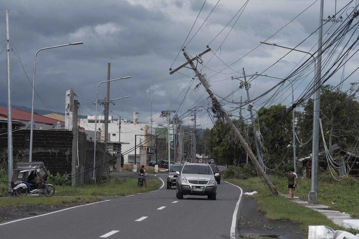 Vehicles pass by toppled electrical poles as Typhoon Kammuri slams Legazpi city.
