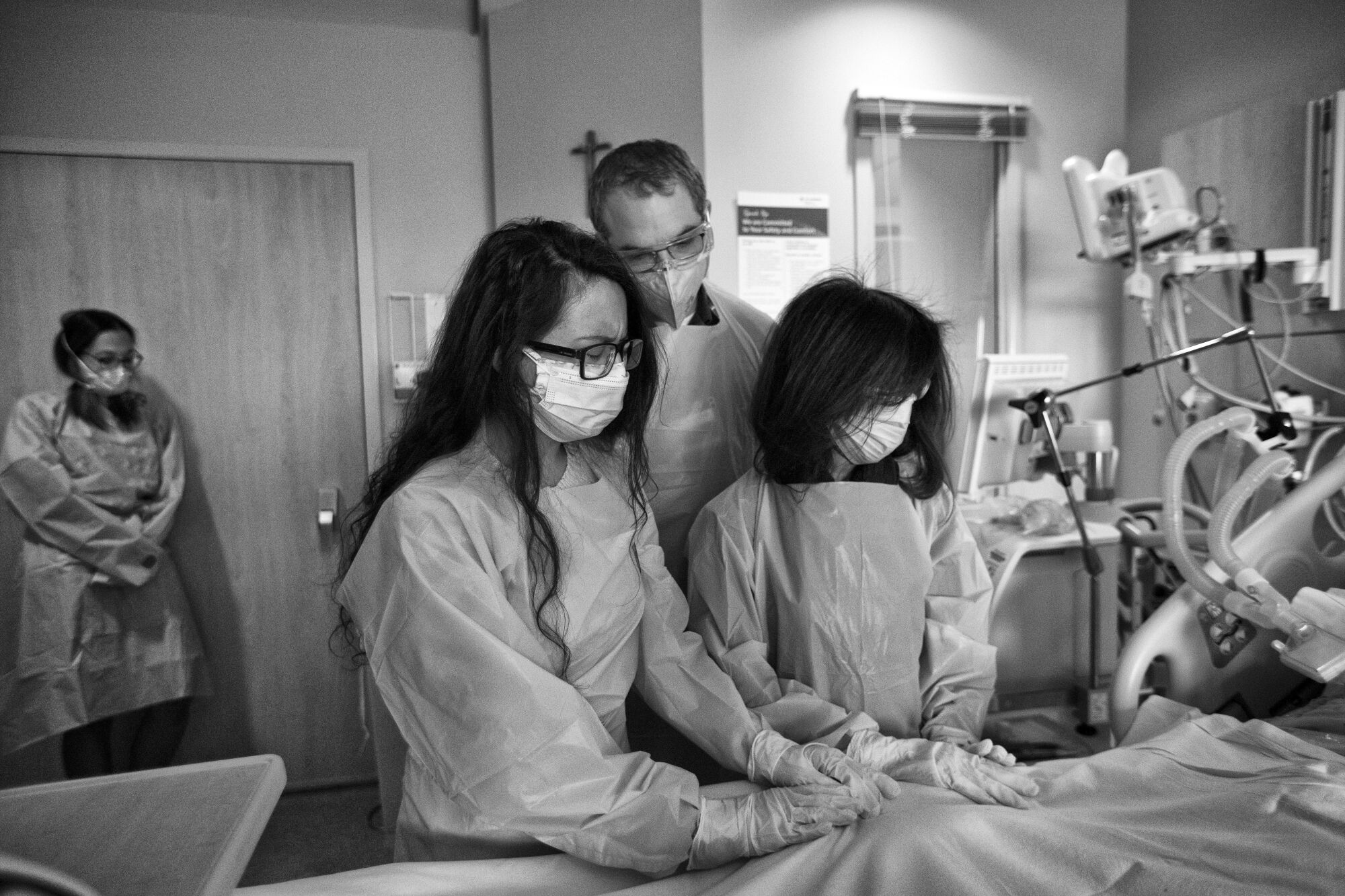 Three people standing at the bedside of a hospital patient
