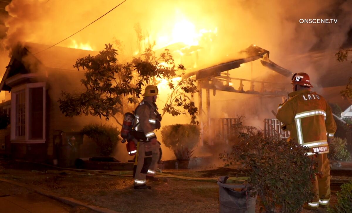 Two firefighters stand in front of a burning house.