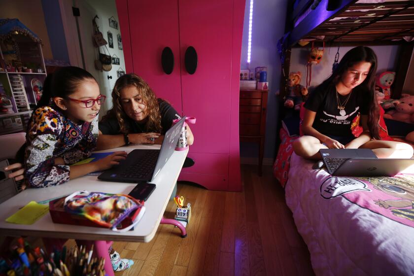 LOS ANGELES, CA - SEPTEMBER 17: 9-year-old Priscilla Guerrero uses a laptop computer for her 4th grade Los Angeles Unified School District online class in her room as mom Sofia Quezada assists her and 13-year-old sister Paulette Guerrero during remote learning lessons at home on September 17, 2020. Boyle Heights on Thursday, Sept. 17, 2020 in Los Angeles, CA. (Al Seib / Los Angeles Times