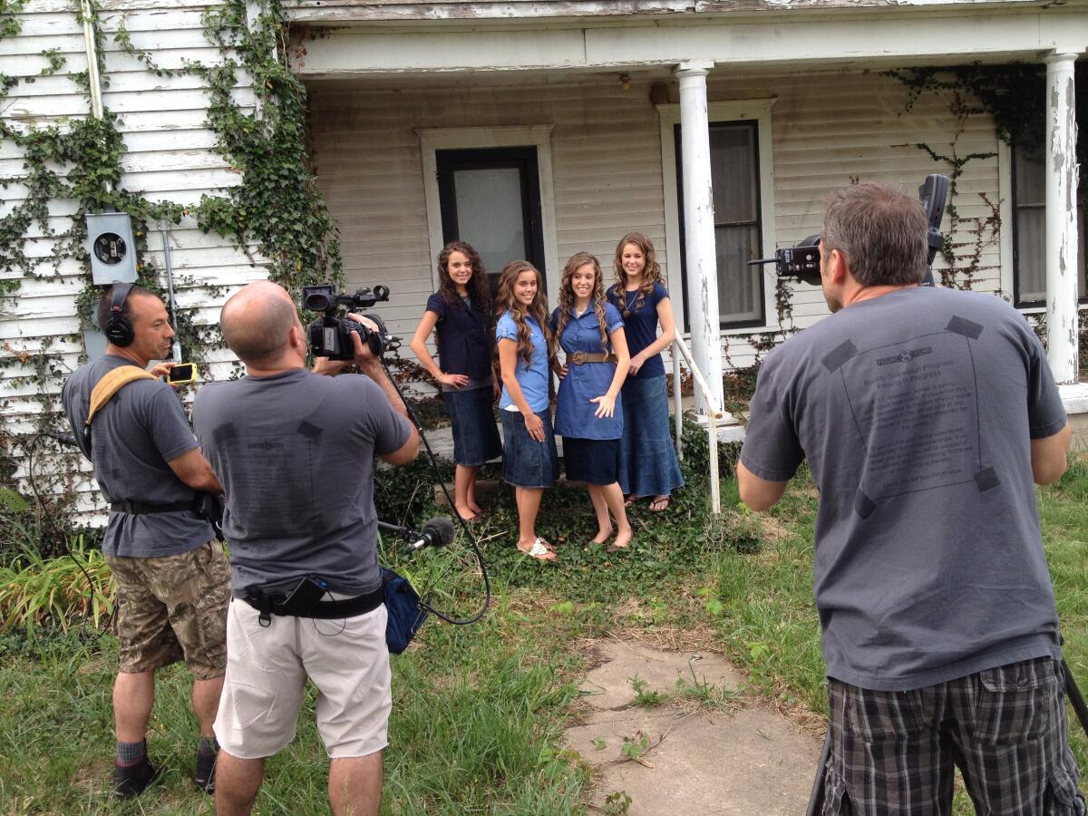 Jinger, Jessa, Jill and Jana Duggar standing in front of a house as photographers point their cameras at them.