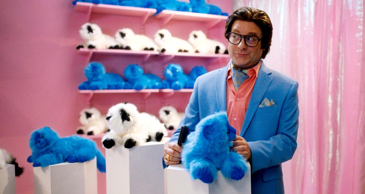 A man in a blue suit stands among stuffed animals in a pink room