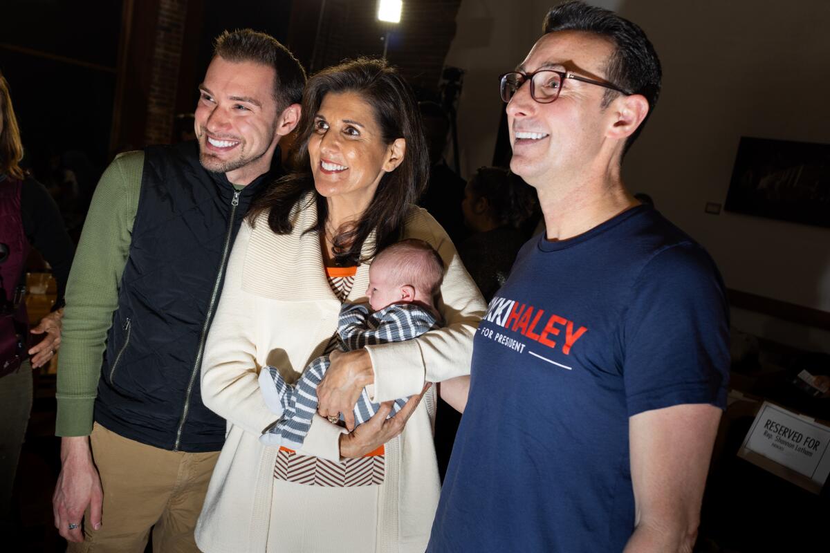 Nikki Haley poses for a photo holding a baby and standing between two men