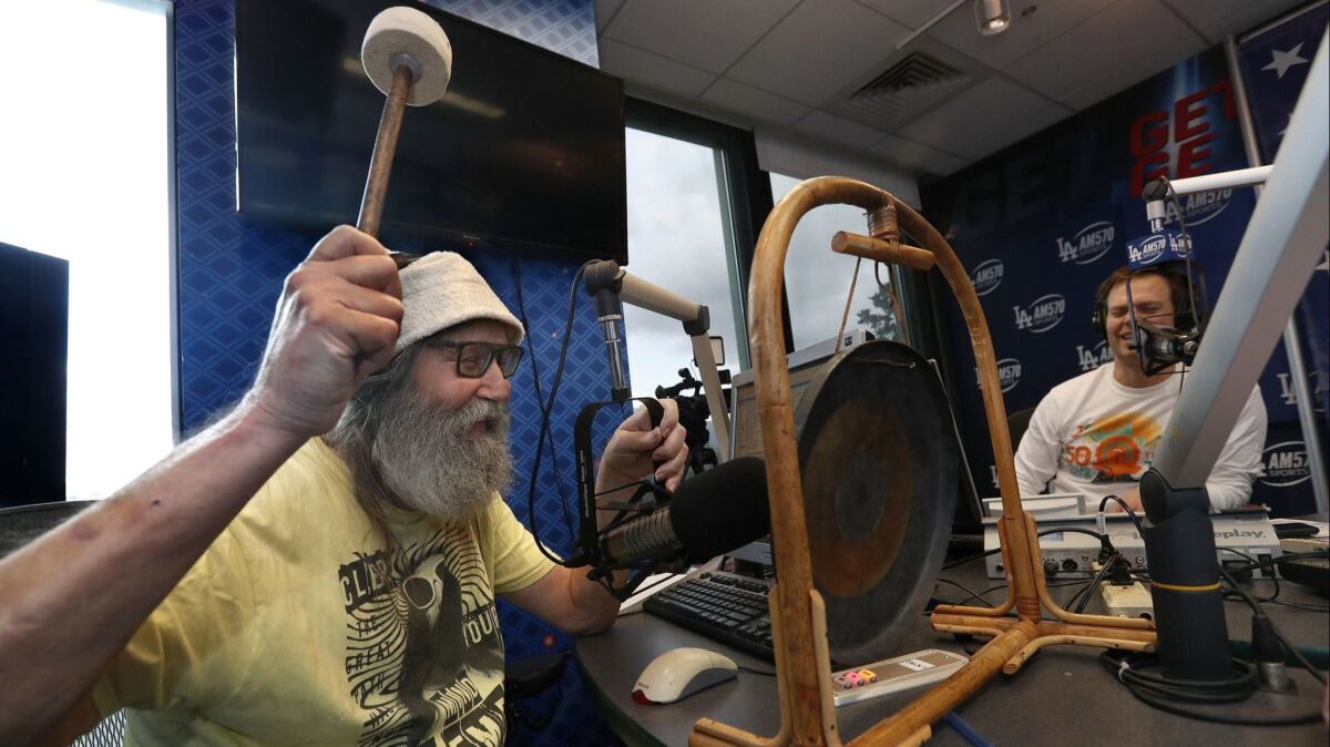 Radio sports announcer Vic "the Brick" Jacobs strikes the gong while giving a sports update on the radio show, "Petros and Money" at iHeartMedia in Burbank. At right is radio sports personality Matt "Money" Smith.