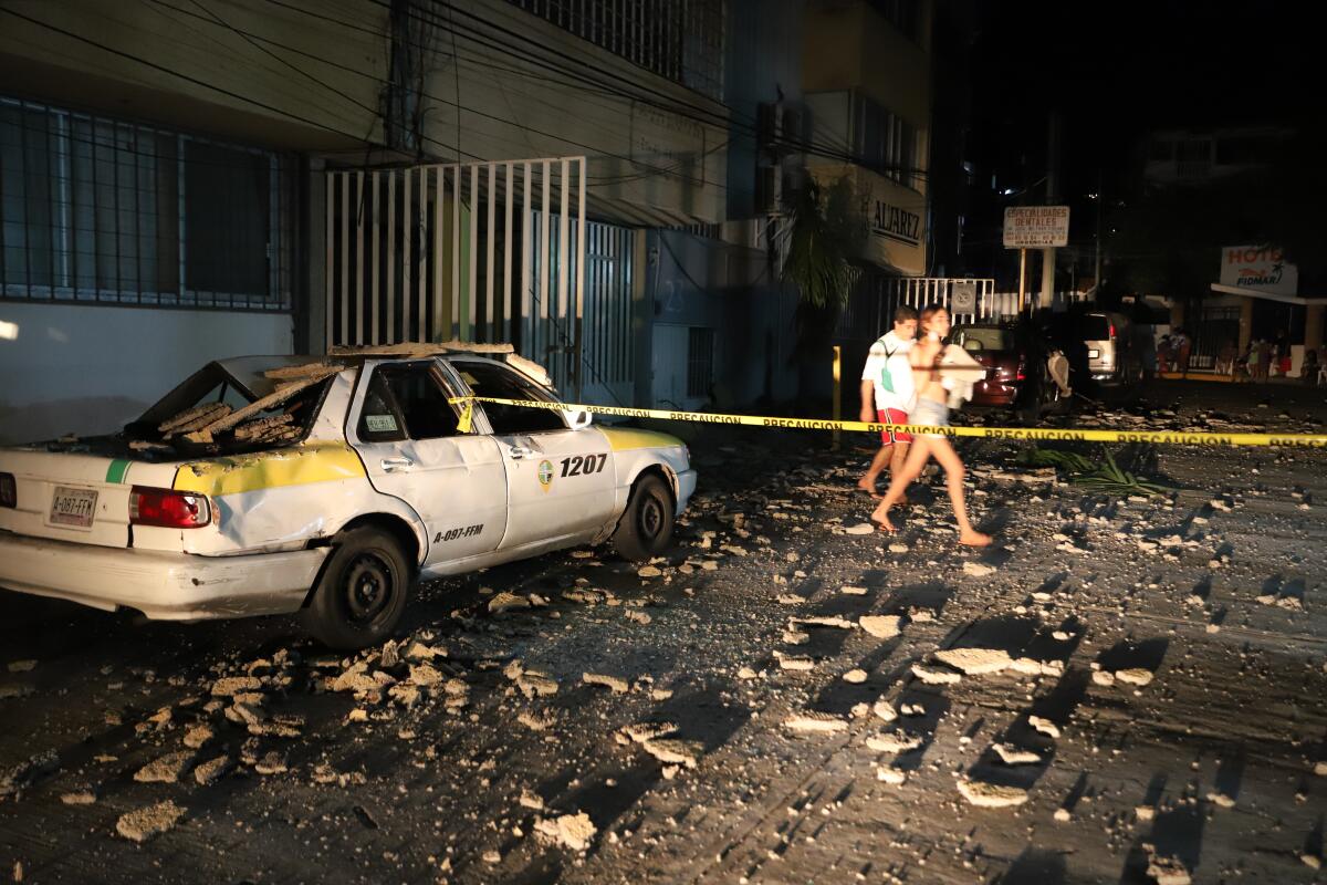 A couple walks past a taxi cab that was damaged by falling debris after a strong earthquake in Acapulco, Mexico, Tuesday, Sept. 7, 2021. The quake struck southern Mexico near the resort of Acapulco, causing buildings to rock and sway in Mexico City nearly 200 miles away. (AP Photo/ Bernardino Hernandez)