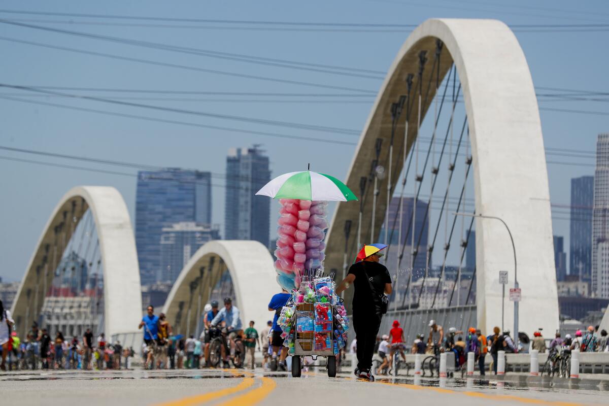 A street vendor joins pedestrians and cyclists on a bridge, with skyscrapers in the background 