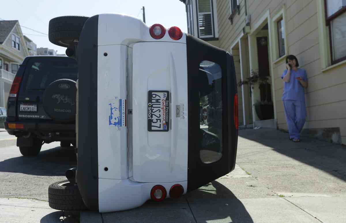 Shelley Gallivan, right, talks on the phone next to a tipped over Smart car, which belongs to her friend, in San Francisco on Monday, April 7, 2014.