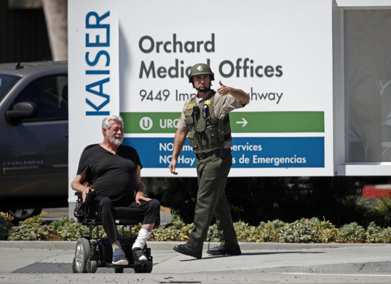 A man in a wheelchair and a Los Angeles County Sheriff's deputy wait outside Kaiser Permanente Downey Medical Center after reports of someone with a weapon at the facility.
