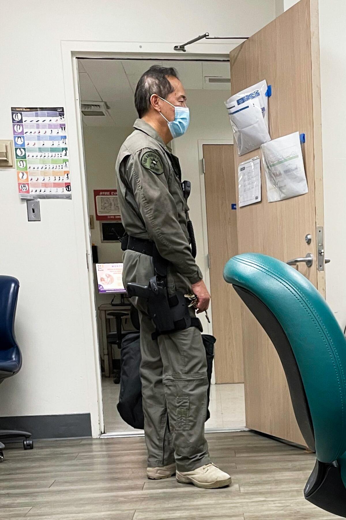 Dr. Louis Kwong stands in a doorway with a gun on his hip.