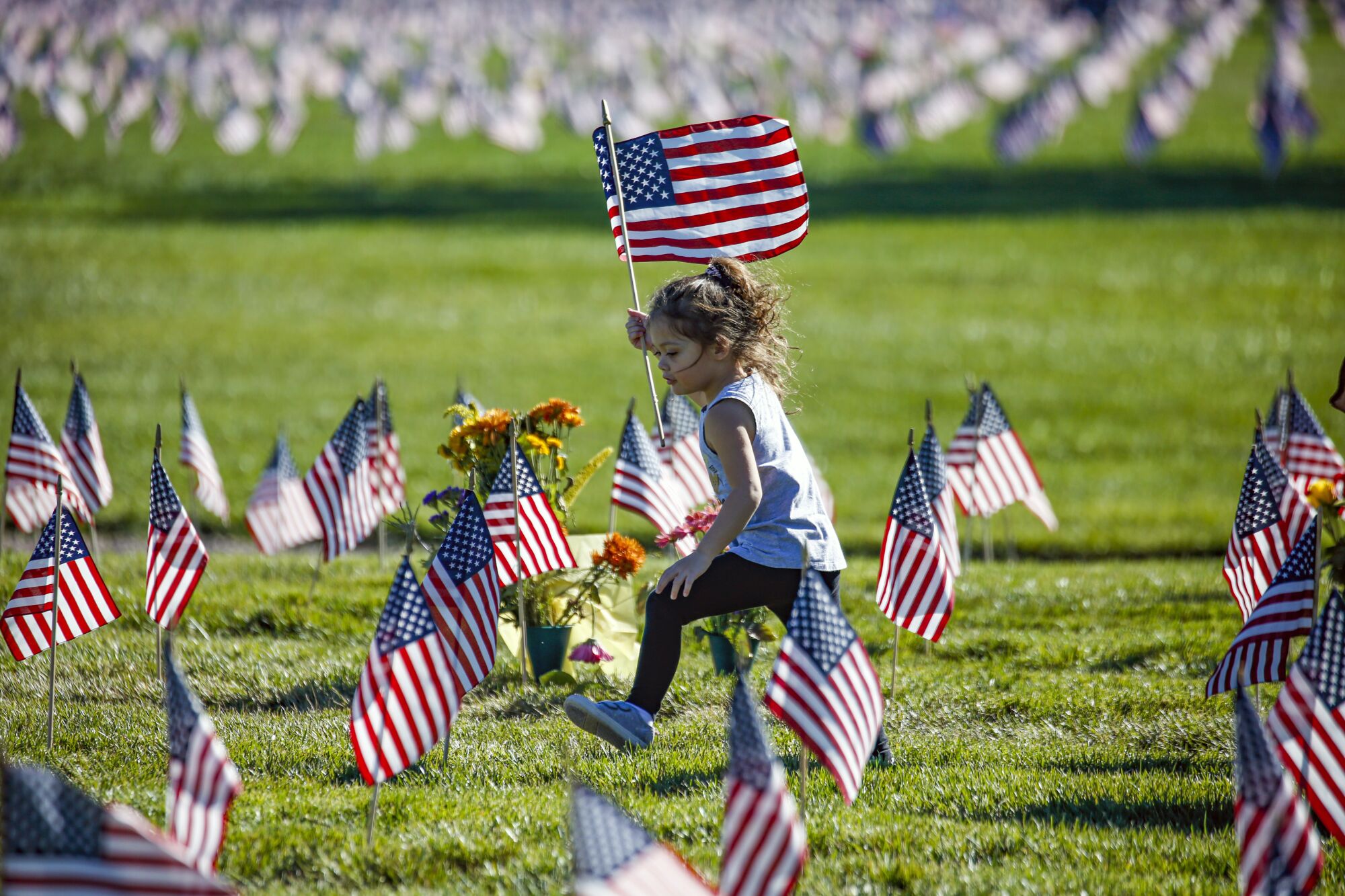 A young girl carries a U.S. flag while running among small flags planted in the grass